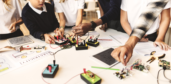 Close-up shot of the hands of the instructor and students from before, working on mechanical projects in the library.